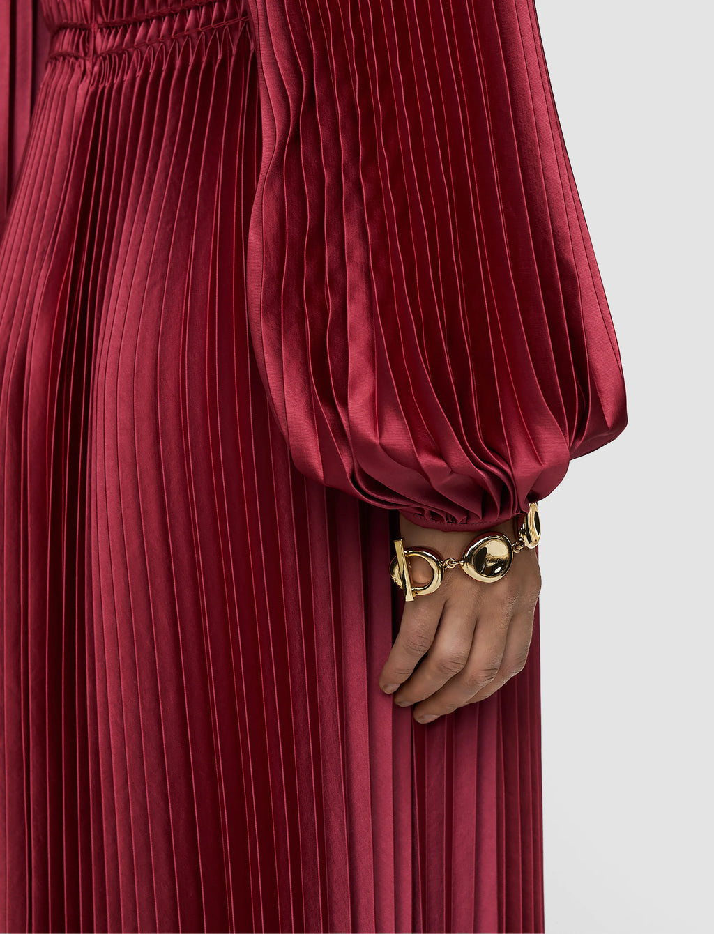 Red pleated dress with a gold bracelet on a neutral background