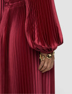Red pleated dress with a gold bracelet on a neutral background