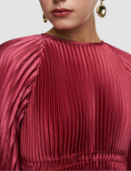 Close-up of a person wearing a pleated red dress with gold earrings on a light gray background