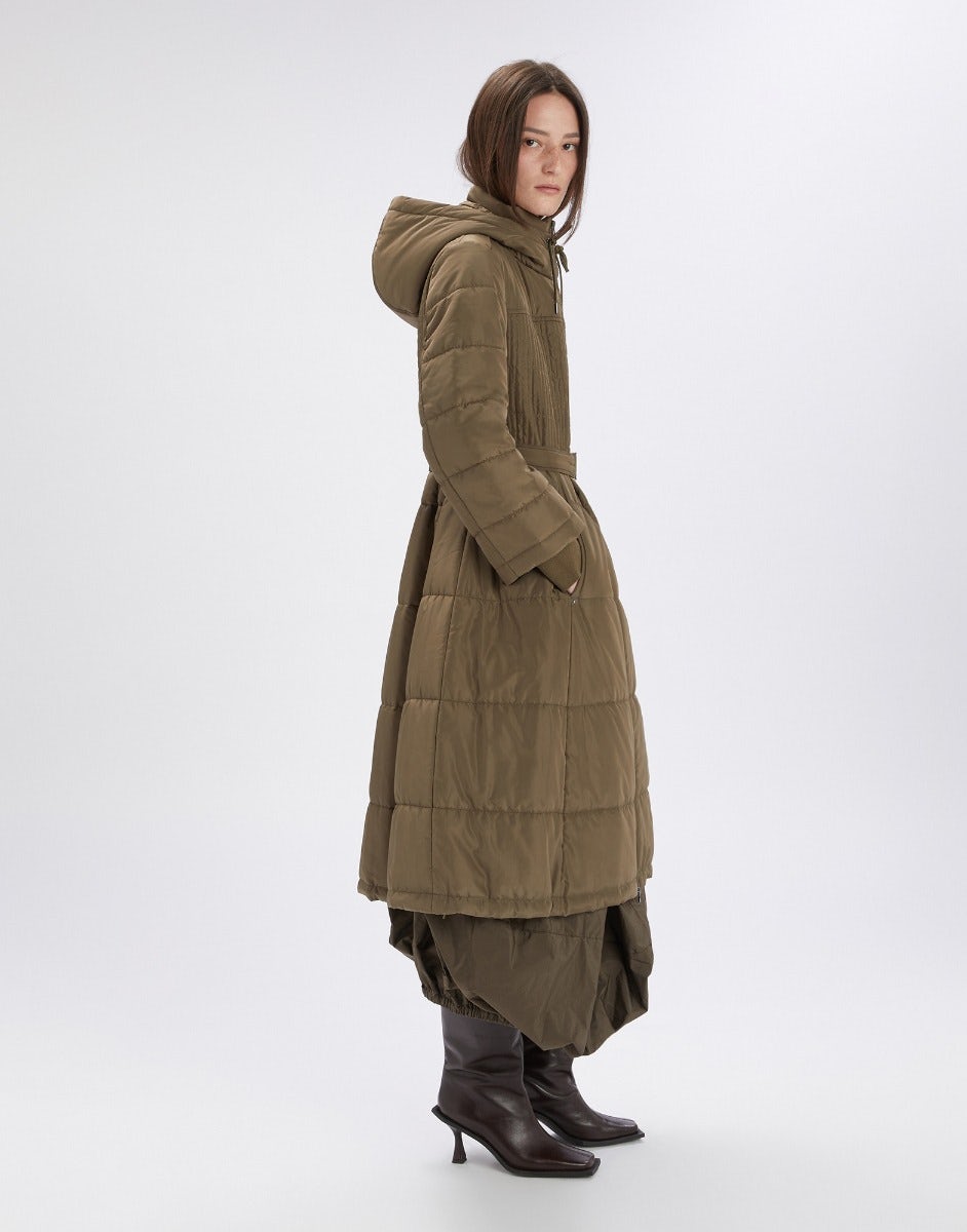 Woman wearing a long olive green coat on a white background