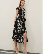 A model wearing a black floral wrap-dress with a belted waist, crossover V-neckline, and in-seam pockets. The dress features a fit-and-flare silhouette.