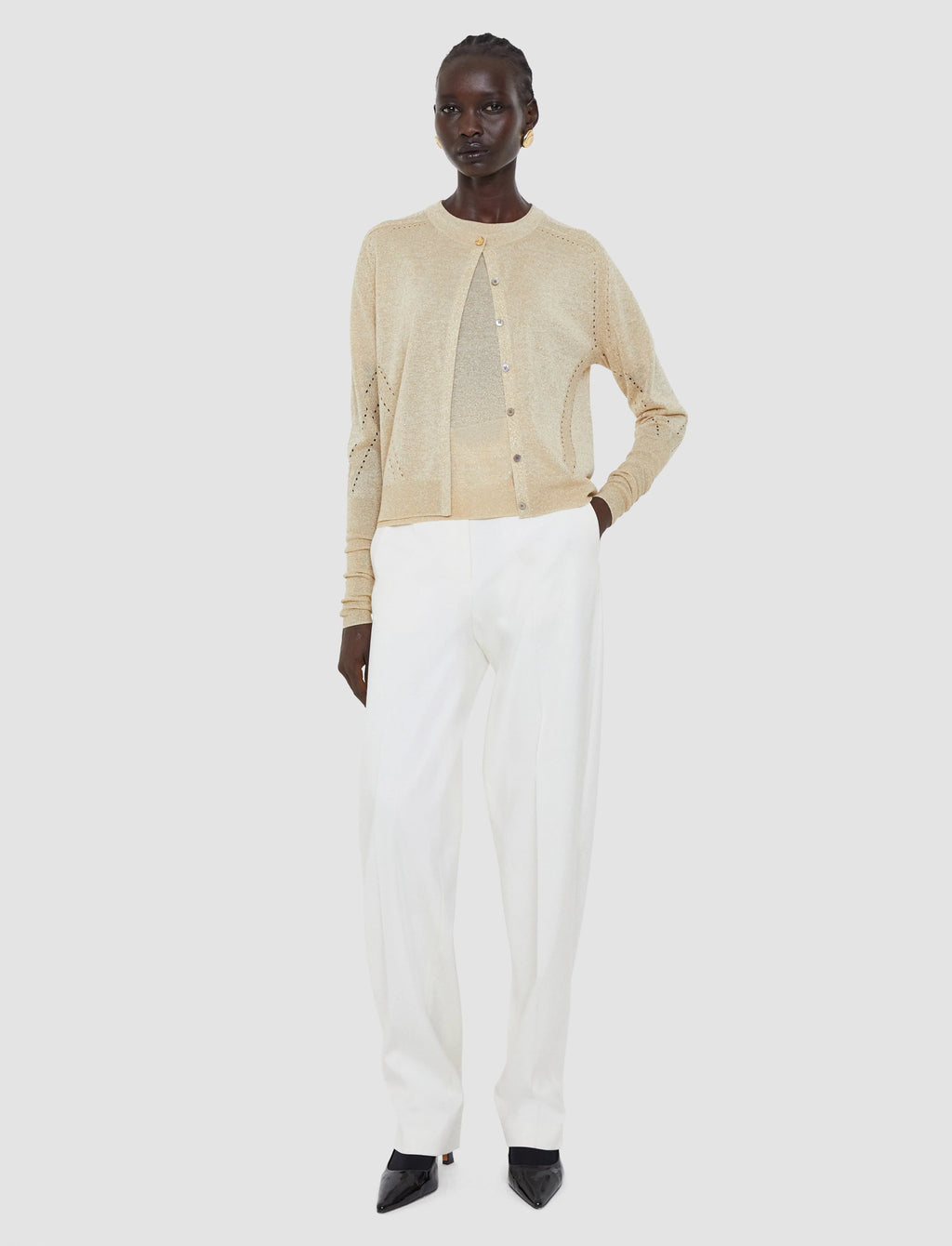 Person wearing a beige cardigan and white pants on a white background