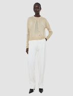 Person wearing a beige cardigan and white pants on a white background