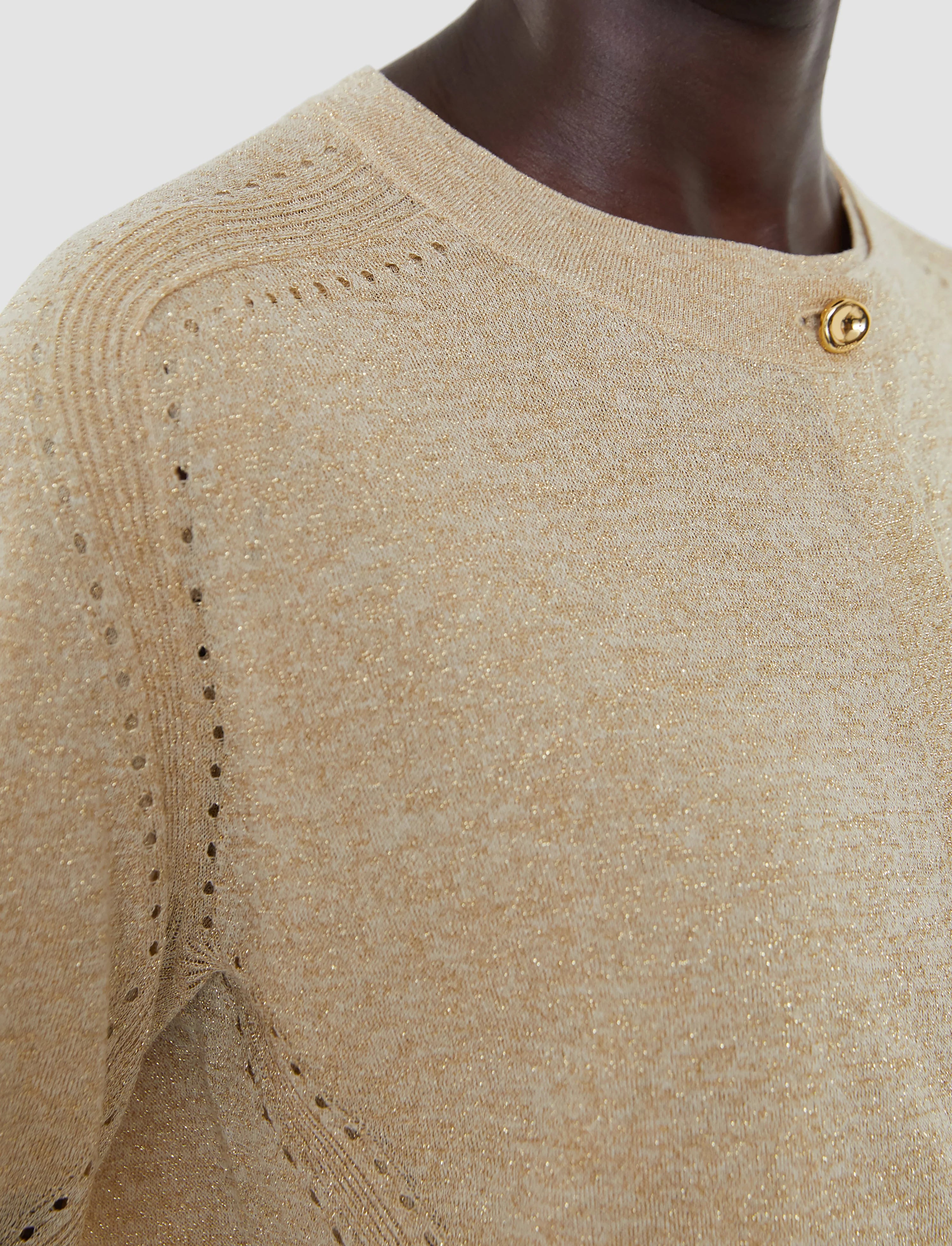 Close-up of a beige sweater with a textured pattern and gold buttons on a neutral background
