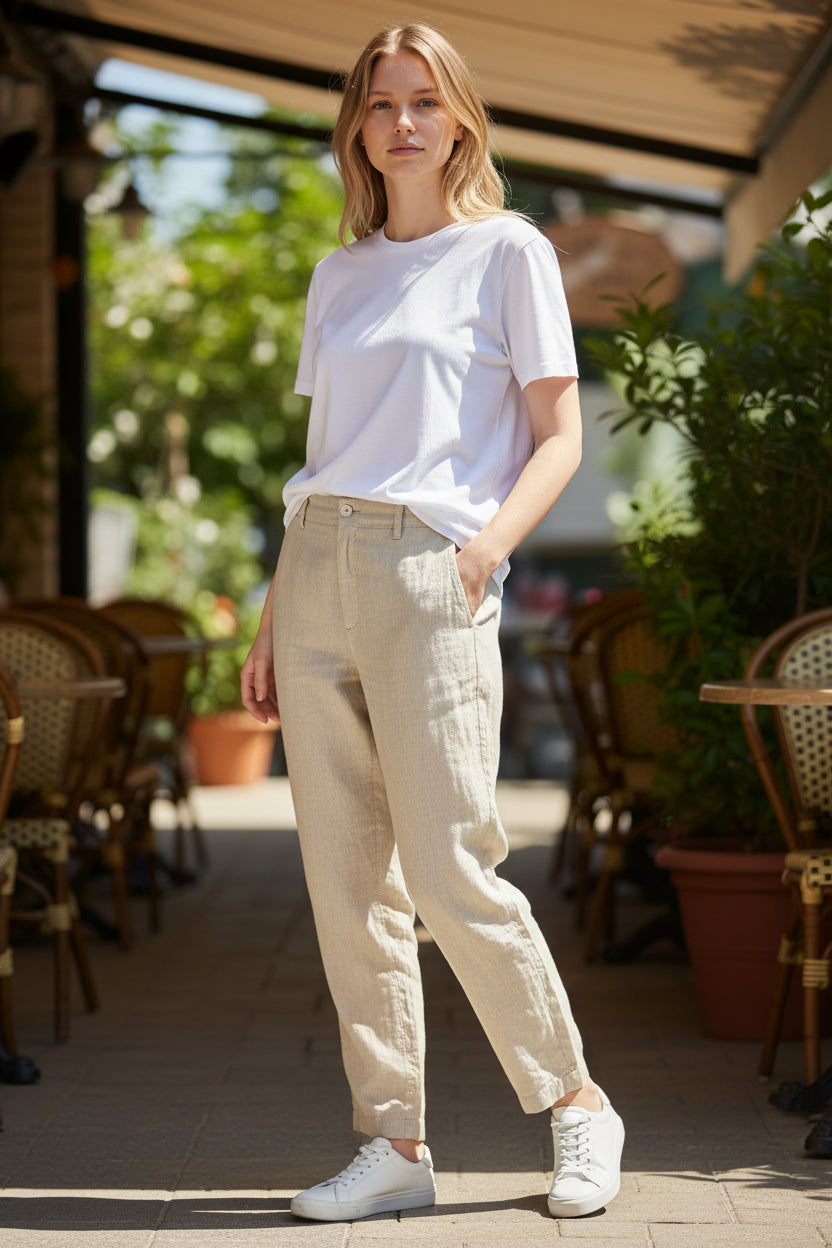 Woman wearing a white t-shirt and beige pants standing in an outdoor setting with tables and chairs.