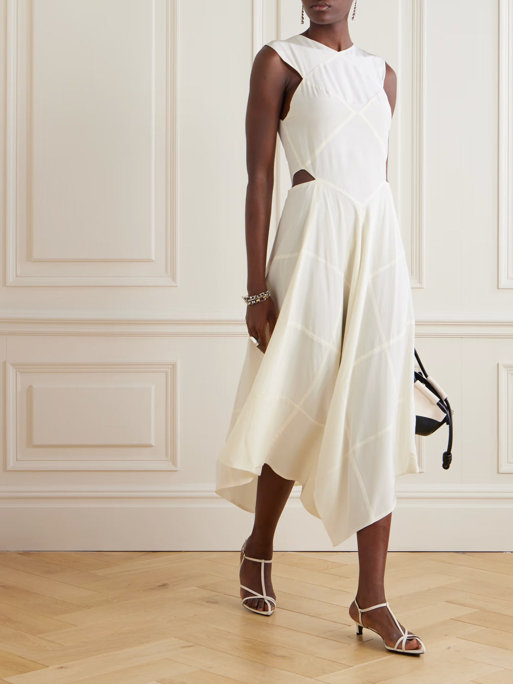 Woman wearing a white dress standing against a white paneled wall.