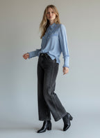 Woman wearing a light blue shirt and black jeans against a plain background