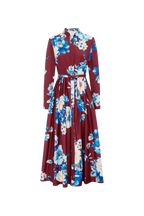A long-sleeved maxi dress with a high collar and a matching waist tie, featuring a bold floral print in blue, cream, and white over a deep burgundy base, shown against a plain white background.