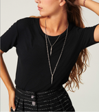 A woman wearing a black ba&sh Merena T-shirt with a crew neck and short sleeves, paired with a skirt and layered necklaces.